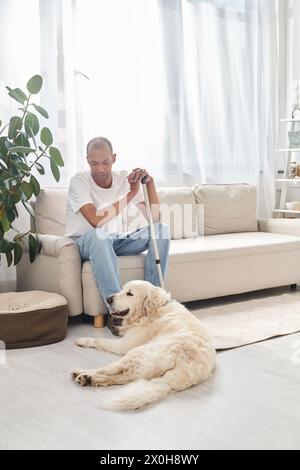 A disabled African American man with myasthenia gravis relaxes on a couch with his loyal Labrador dog, promoting diversity and inclusion. Stock Photo