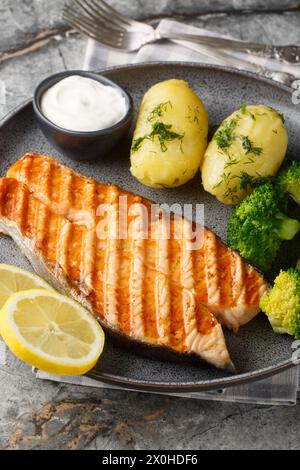 Grilled salmon steak with new potatoes, broccoli and cream sauce close-up in a plate on the table. Vertical Stock Photo