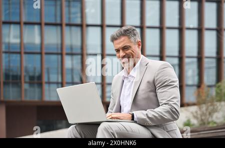 Happy busy middle aged business man working on laptop outside office. Stock Photo