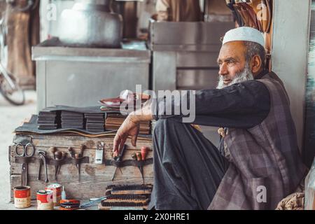 Poor old Pakistani Pathan shoe man cobbler on the local streets of Pakistan with his hand made leather shoes and repair tools in his street shop Stock Photo