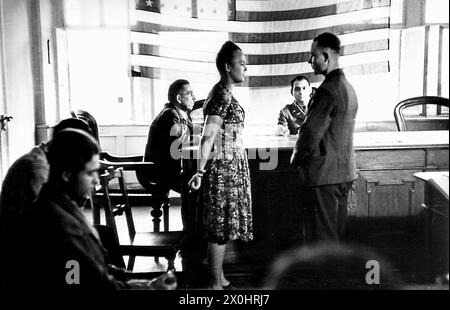 A young German woman in dress is sworn in by the US Lieutenant Feld in front of an American flag in Ochsenfurt.  She had applied to be a civilian employee of the American troops and now she makes her oath of service. Stock Photo