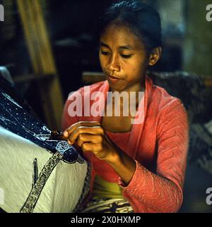 A young woman applies a pattern onto a cloth using liquid wax in batik technique [automated translation] Stock Photo