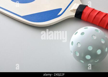 Detail of pickleball racket and a white ball isolated on white table. Elevated view. Stock Photo