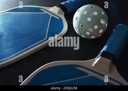 Two blue wooden paddle pickleball rackets and a white ball on black table. Elevated view. Stock Photo