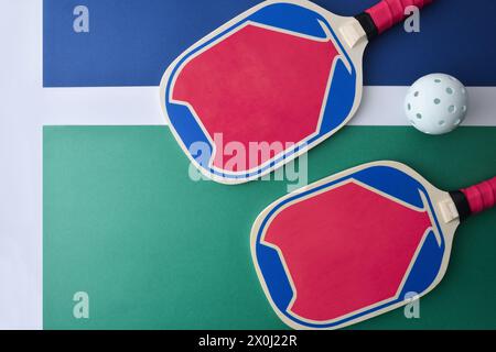 Blue and pink wooden pickleball paddles and a white ball on playing court. Top view. Stock Photo