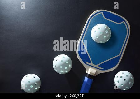 Background with blue wooden pickleball paddle and four white balls on a black table. Top view. Stock Photo