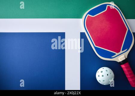 Pickleball background with wooden blue and pink racket with white ball on playing court. Top view. Stock Photo