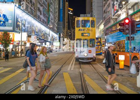 Causeway Bay at night with a yellow tram in the road and people crossing the crosswalk. Hong Kong - 28th August 2023 Stock Photo