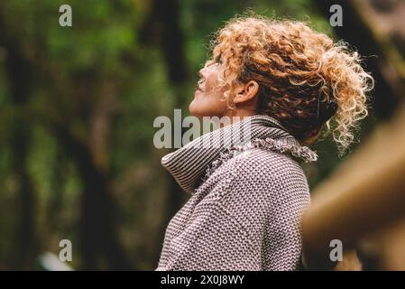 Side portrait of woman relaxing in the nature. Inner balance and mindfulness concept moments. Standing female people in the woods enjoying silence and good nature vibes alone smiling and admiring Stock Photo