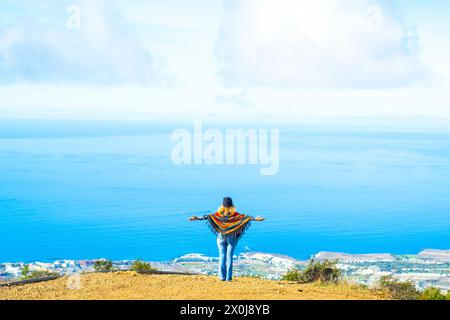 Tourist and freedom lifestyle people travel concept. Woman viewed from back opening arms to enjoy an amazing view and landscape. Blue ocean and sky from a top of a cliff. Happy lady Stock Photo