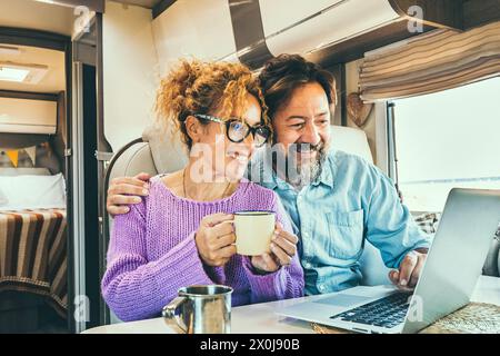 Modern couple use together laptop inside camper van. Computer leisure people surfing the web. Traveler planning next destination smiling and enjoying freedom living off grid. Digital nomad concept Stock Photo