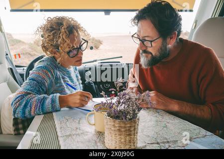 Adult couple planning next travel destination sitting inside a camper van using a paper map guide on the table. ature traveler and vanlife alternative people lifestyle. Couple of tourist and beach view Stock Photo
