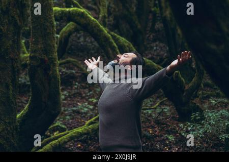 Spiritual zenlike nature love people. One man with closed eyes and outstretching arms in the nature forest green trees scenic place. Travel destination. Natural care medicine therapy. Adventure life Stock Photo