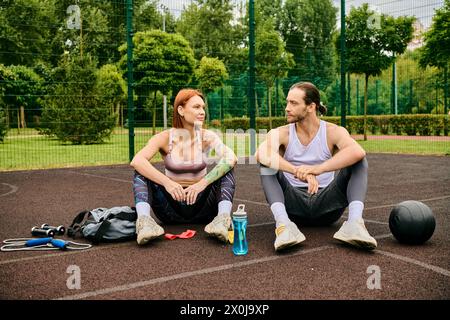 A woman, in sportswear, sit on a basketball court, guided by a personal trainer with determination and motivation. Stock Photo