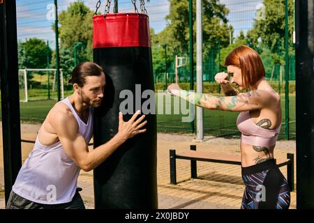 A woman in sportswear engage in a boxing workout in a park, guided by a personal trainer, showcasing determination and motivation. Stock Photo