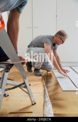 Two mature men installing laminate flooring in a new home together. DIY concept. Professional renovation of a house. Stock Photo