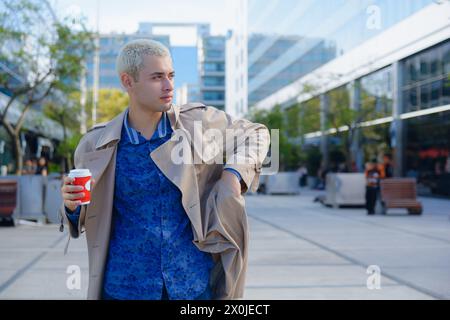 young blond man in argentina entrepreneur standing outside commercial buildings standing taking out mobile phone from jacket, business concept with co Stock Photo