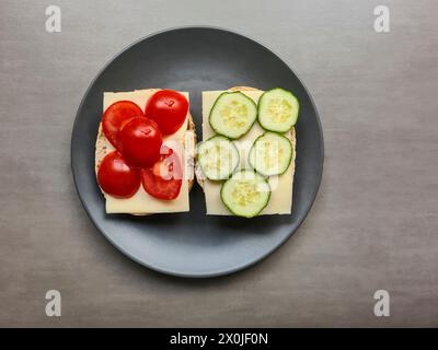 Two slices of bread topped with cheese, cucumber and tomato, sliced Stock Photo