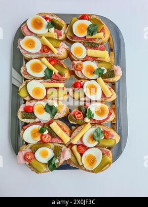 Serving platter with plenty of toppings such as tomatoes, cheese, gherkins, egg slices and cooked ham on bread as an appetizer Stock Photo