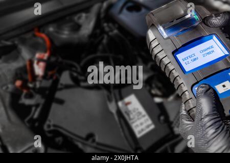 Explore automotive diagnostics as a mechanic holds a battery tester under the hood, displaying Defect and Change on the screen above the car battery, Stock Photo