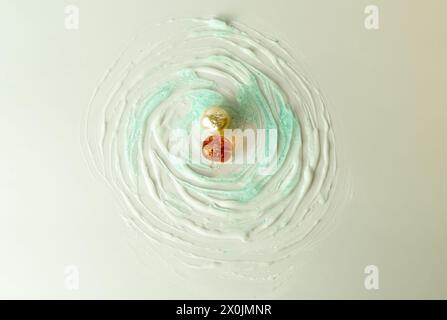 two pearls, one white and one ochre, located in the centre of white and blue concentric circles like waves of water, on a white background Stock Photo