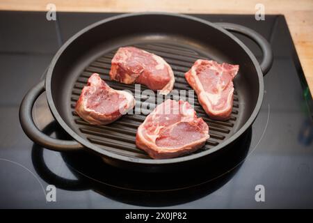 Four lamb chops cooking on a griddle pan on a hob Stock Photo