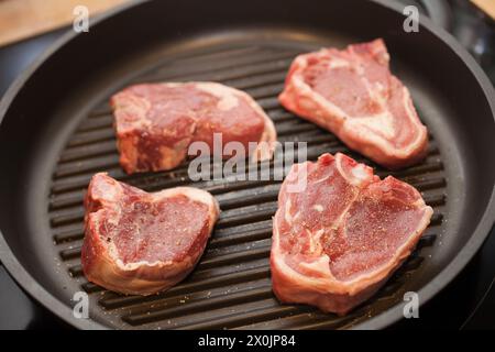 Four lamb chops cooking on a griddle pan on a hob Stock Photo