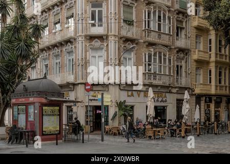 Terrace of a bar with people sitting on chairs and tables with an old kiosk and monumental ficus in a corner of Plaza San Francisco, Cartagena Stock Photo