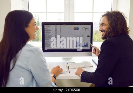 Two cheerful colleagues in office are discussing joint work project and analyzing financial graphs. Stock Photo