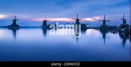 Windmills reflecting in water at sunset, creating a serene natural landscape Stock Photo