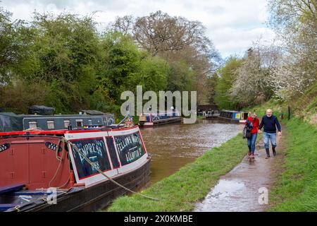 Couple walking along the towpath of the Shropshire union canal passed moored narrowboats in the Cheshire village of Audlem England UK Stock Photo