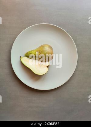 A halved pear with stem lies with both halves on a light gray plate, theme healthy natural nutrition with fruit Stock Photo