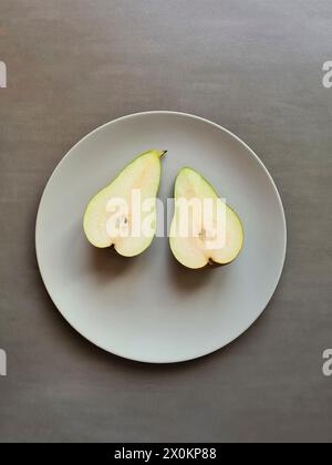 A halved pear with stem lies with both halves on a light gray plate, theme healthy natural nutrition with fruit Stock Photo