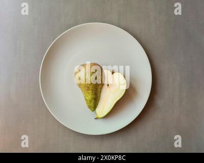 A halved pear with stem lies with both halves on a light gray plate Stock Photo