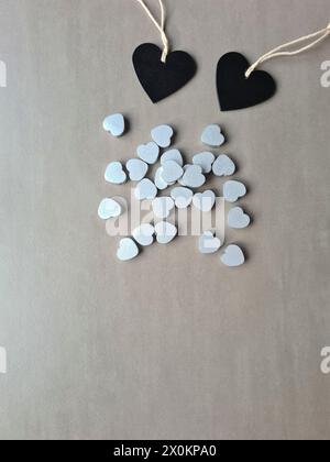 Two black wooden hearts lie next to many small silver-colored hearts Stock Photo