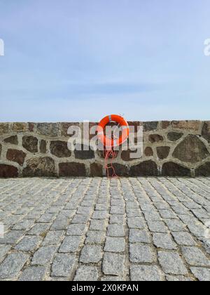 A red lifebuoy with reflective stripes and lifeline hanging on a quay wall, Sassnitz town harbor, Germany Stock Photo