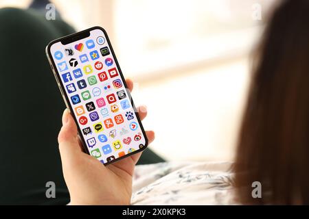 KYIV, UKRAINE - APRIL 1, 2024 Many apps icon on smartphone screen in young female hands indoors. Woman using iPhone app at home Stock Photo