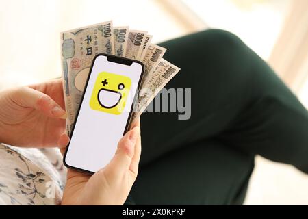 KYIV, UKRAINE - APRIL 1, 2024 Hago icon on smartphone screen and money in female hand. iPhone display with app logo and japanese yen money bills in women hands close up Stock Photo