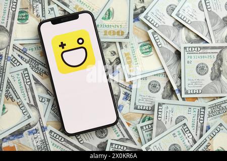 KYIV, UKRAINE - APRIL 1, 2024 Hago icon on smartphone screen and many usd money bills. iPhone display with app logo and lot of hundred dollars banknotes close up Stock Photo