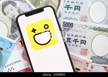 KYIV, UKRAINE - APRIL 1, 2024 Hago icon on smartphone screen on many asian money bills. iPhone display with app logo with japanese yen and chinese yuan banknotes Stock Photo
