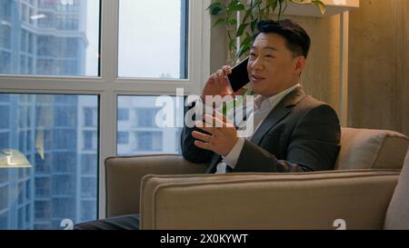 Asian happy businessman chinese japanese man calling mobile phone sit in office modern company smiling ethnic middle-aged entrepreneur employee worker Stock Photo