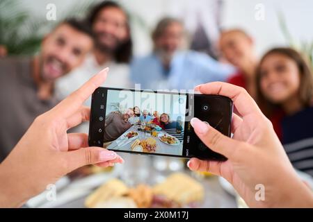 POV smart phone hold by unrecognizable woman taking photo Caucasian family in meal together. Stock Photo