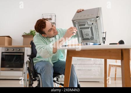 Young man in wheelchair repairing microwave oven at home Stock Photo