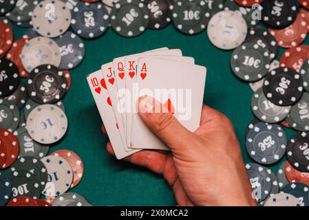 Royal flush in the game of poker in the hands of the player on the background of a green table with gaming chips in the casino Stock Photo