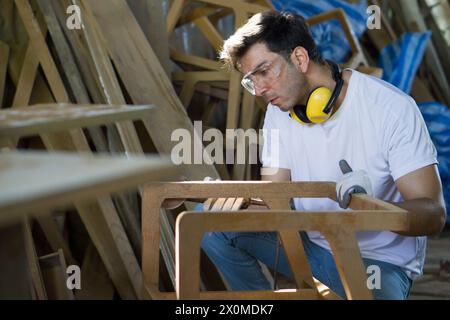 A man is focused as he shapes a piece of wood with his tools in a workshop setting. Side view Stock Photo