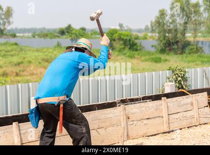 Worker hit pile for reinforce formwork building concrete foundation for new fence. Stock Photo