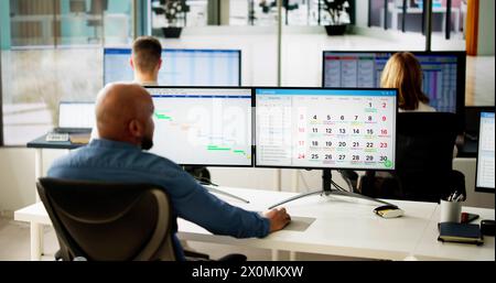 Young Businesspeople Analyzing Gantt Chart And Calendar On Computer In Office Stock Photo