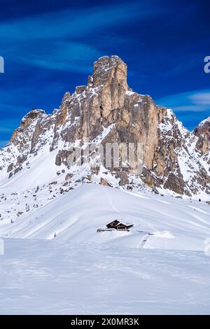 Snow-covered slopes of alpine Dolomite landscape around Giau pass in winter, the summit of Ra Gusela and a mountain hut in the distance. Stock Photo