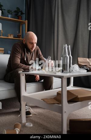 Handsome depressed man drinking whisky or brandy at home sitting on sofa in living room. Alcoholism and depression Stock Photo