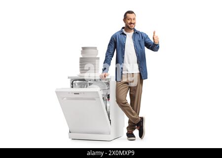 Guy showing thumbs up next to a dishwasher and a pile of clean white plates isolated on white background Stock Photo